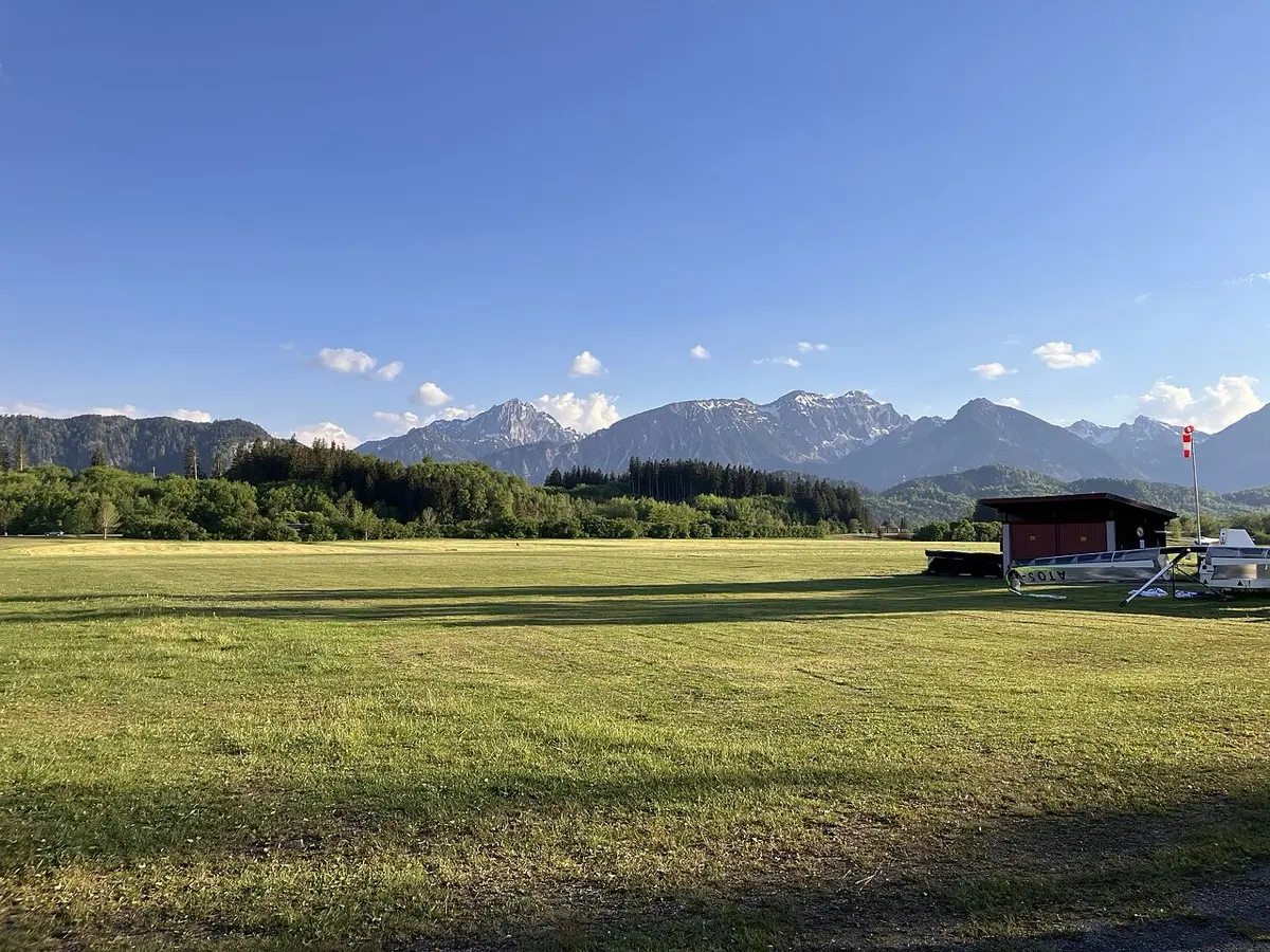 Leere Graspiste mit Hütte und Windsack, dahinter die Alpen
